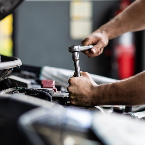 Mechaniker arbeitet mit einer Ratsche am Motor eines Fahrzeugs – Unfallgutachten